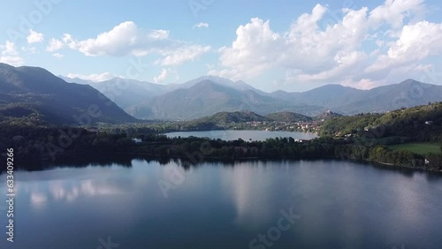 Bird eye view of two lakes called Laghi di Avigliana. Aerial drone view of lakes with calm water surrounded by mountain ranges in Italian Alps in summer. Water surface reflects clouds, Piedmont, Italy