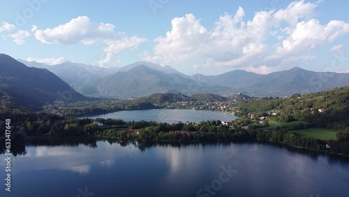 Bird eye view of two lakes called Laghi di Avigliana. Aerial drone view of lakes with calm water surrounded by mountain ranges in Italian Alps in summer. Water surface reflects clouds, Piedmont, Italy