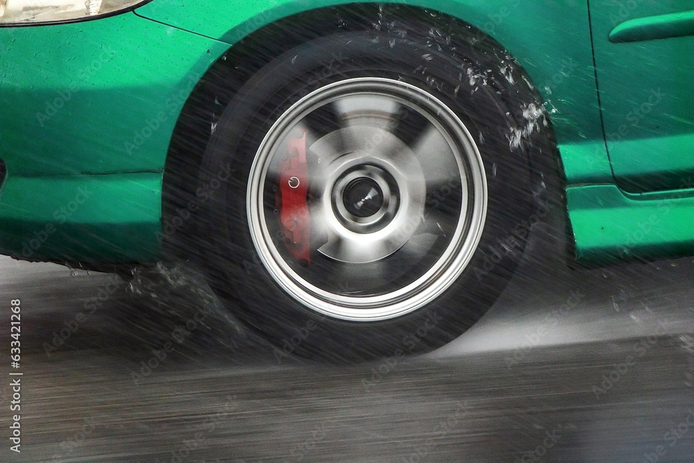 Detail of the rear wheel of a car driving in the rain on a wet road. Aquaplaning in road traffic. Detail of the rear wheel of a car driving in the rain on a wet road. Aquaplaning in road traffic.