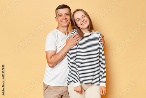 Happy joyful smiling positive man and woman wearing casual clothing standing isolated over beige background hugging looking at cmaera wxpressing happiness. photo