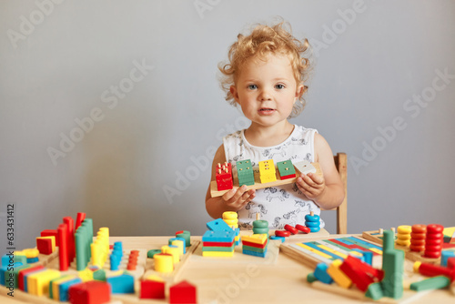 Infants' joyful learning experiences. Toddler's curious exploration. Child's imaginative playtime. Funny wavy haired blonde toddler baby playing wooden educational toys isolated over gray background