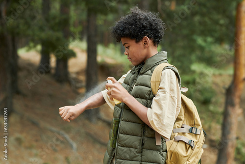 African American boy applying mosquito spray during hiking outdoors
