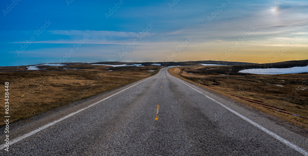 Asphalt road in beautiful tundra landscape with dry grass and some snow