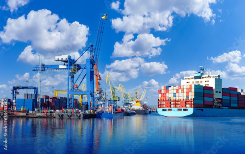Ship in seaport. Sea vessel with containers on board. Cargo harbor with cranes for loading. Seaport on sunny day. Ship with containers on background blue sky. Port for loading ships. Modern seaport