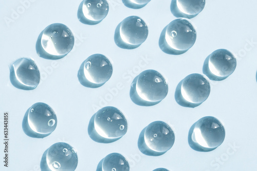 Hyaluronic transparent drops on a blue background, top view. Beauty background with a pattern of liquid cosmetic product stains.