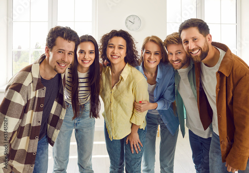 Group of happy smiling funny friends students or colleagues in casual clothes standing together and looking cheerful and positively at the camera. Portrait of friendly guys and girls indoors. photo