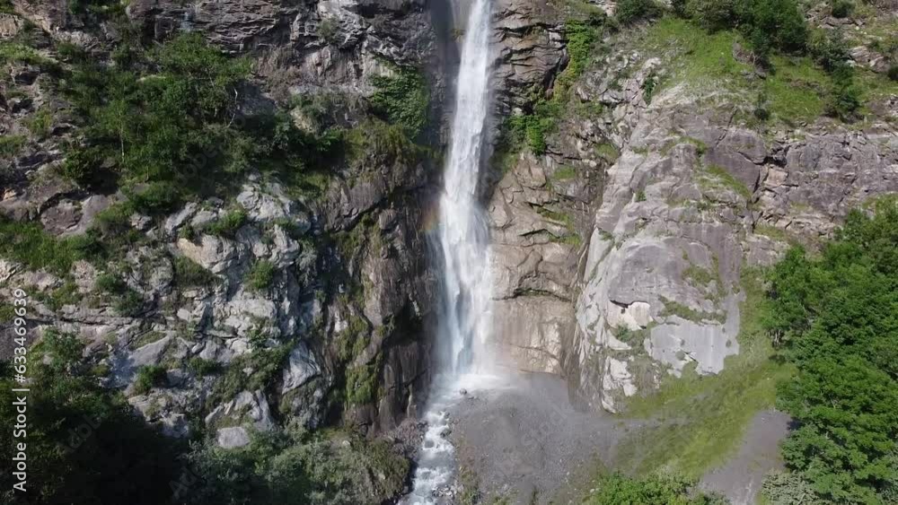 View of waterfall called Cascata Di Novalesa in Italian Alps, Piemonte, Italy. Aerial view from drone of waterfall from bottom to top. Strip of rainbow on splashes of water flow falling between rocks View of waterfall called Cascata Di Novalesa in Italian Alps, Piemonte, Italy. Aerial view from drone of waterfall from bottom to top. Strip of rainbow on splashes of water flow falling between rocks
