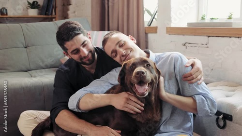 Lovely and relaxed homosexual couple, men sitting on couch at home in living room, hugging and petting the dog. Concept of relationship, happiness, animals, lgbt community