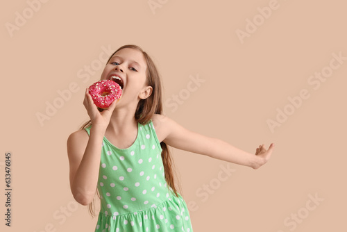 Little girl eating tasty doughnut on beige background