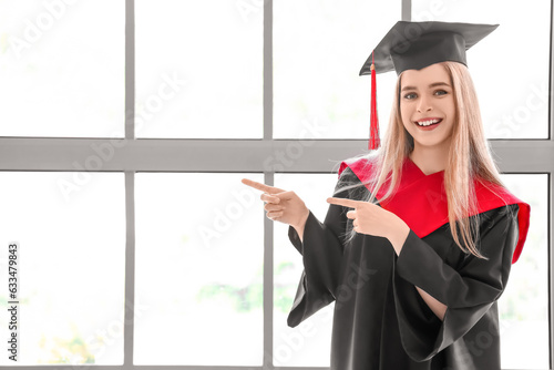 Female graduate student pointing at something near window in room