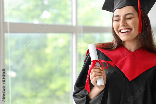 Female graduate student with diploma near window in room
