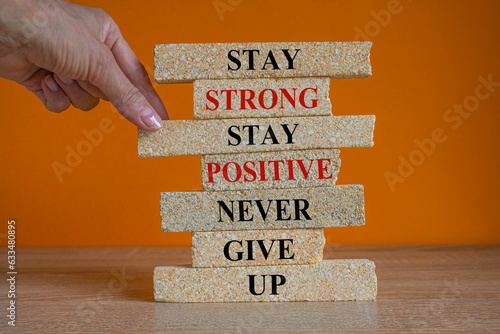 Brick blocks with concept words Stay strong stay positive never give up. Beautiful orange background. Copy space. Businessman hand. Motivational business never give up concept.