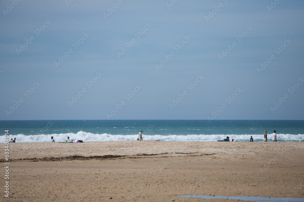 Panoramic view of the beach in the town of conil in cadiz, andalusia, spain. The sky is clear and blue with white clouds. There are people walking and strolling along the seashore.