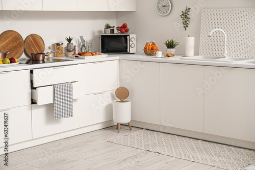 Interior of modern kitchen with stylish rug, trash bin and white counters © Pixel-Shot