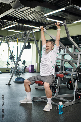 strong and elderly man with beard working out on exercise machine, athletic and healthy, full length