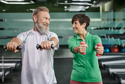 happy elderly couple  happy man and woman training with dumbbells  husband and wife in gym