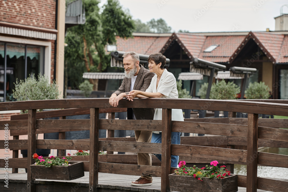 happy senior couple standing together on wooden bridge, elderly love, bearded man and woman happy senior couple standing together on wooden bridge, elderly love, bearded man and woman