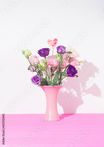 Beautiful fresh Lisianthus flowers in pastel pink vase with ceramic heart shape detail. White pink background. Creative concept of love, wedding, friendship, greetings, birthday, holiday.