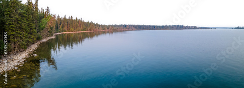 View along the tree covered shore of a large blue colored calm lake with a transparent sky
 photo