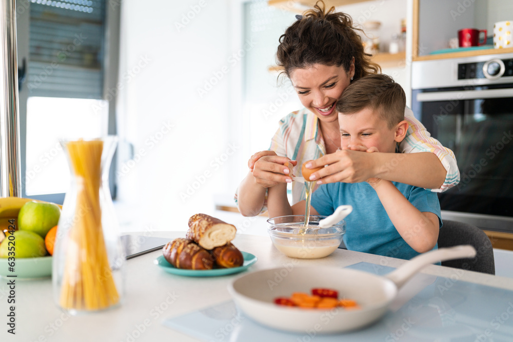 Thrilled and carefree mother and son cracking egg into mixing bowl in the kitchen.