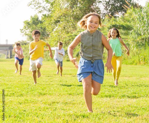 Happy active children running together on green grass in park