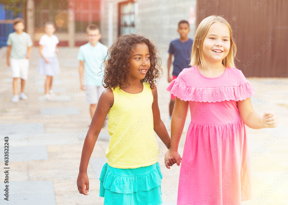 Two positive girls walking hand in hand through streets.