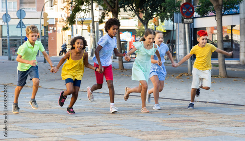 Group of cheerful tweenagers of different nationalities running together along city street on summer day. Happy healthy kids concept..