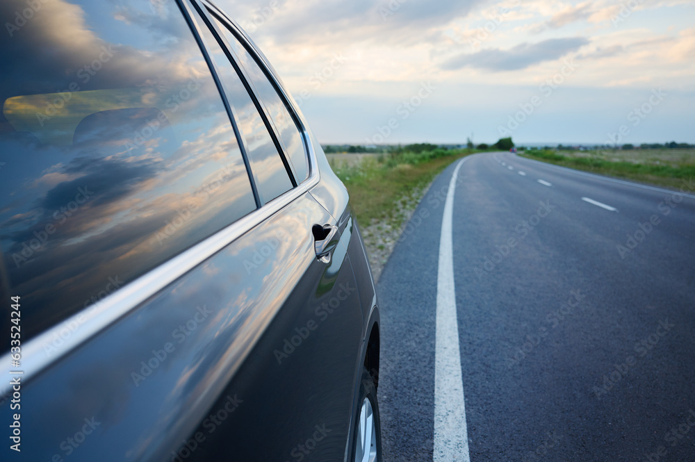 Side view of a car parked next to an asphalt road on the side at sunset outside the city