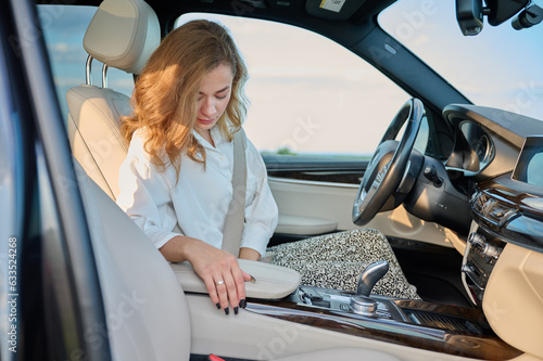 Pretty business lady fastens seat belt in new modern technological car. Happy woman fastening her seatbelt while sitting at the steering wheel of her car. Buckle up and drive safe.