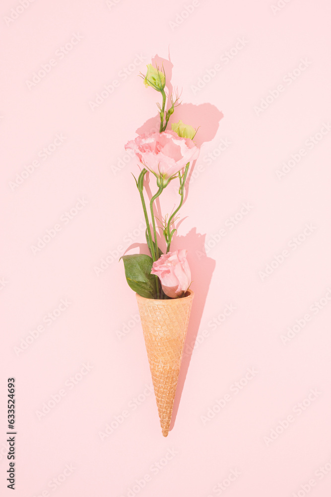 Beautiful flowers are growing out of an ice cream cone. Minimal creative surreal floral concept. Pastel pink color. Copy space. Flat lay.