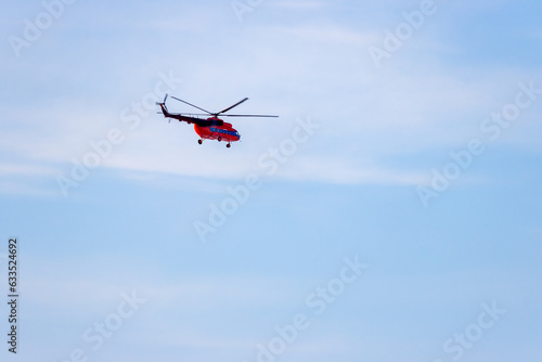 A red helicopter flies against a blue sky. Passenger and cargo air transportation. Aviation transport services. Travel and tourist helicopter flights. Delivery of goods by air.