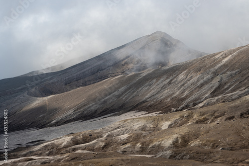 Majestic mountain landscape. View of the top of the volcano. Low clouds. Travel, tourism and hiking on the Kamchatka Peninsula. Nature of the Russian Far East. Gorely volcano, Kamchatka Krai, Russia. photo