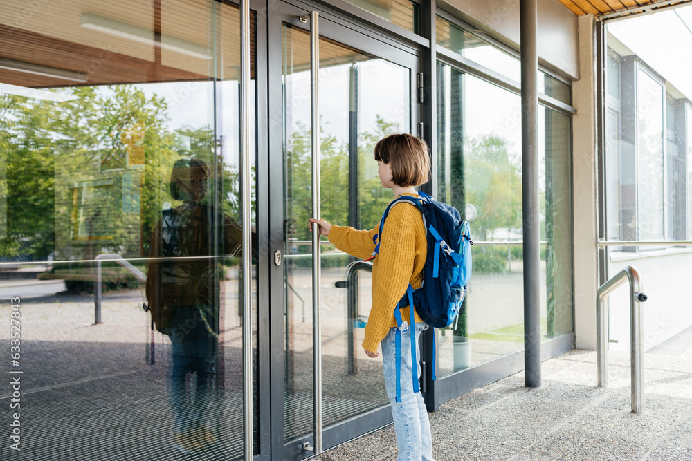 Obraz premium A teenage girl stands in front of the door to the school and opens it. Beginning of lessons and academic year