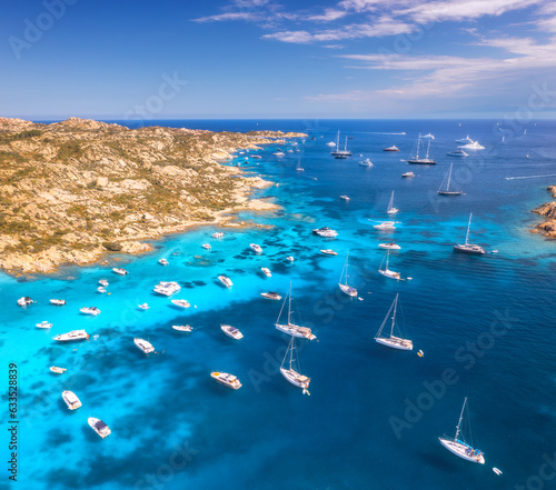Aerial view of luxury yachts and boats on sea bay in sunny summer day. Travel in Sardinia, Italy. Drone view from above of speed boats, yachts, sea lagoon, rocky coast, transparent water. Top view