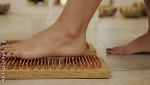 Female feet stand on boards with nails, close up. Barefoot female standing on yoga nails board. Sadhu board