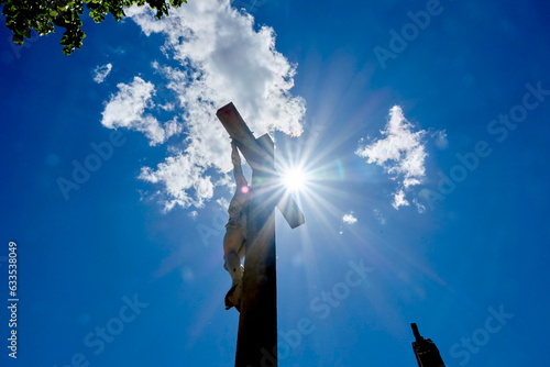 Cross with Jesus Christ from behind and below with clouds in the background, back-lit by a direct view of the sun © Sylvain
