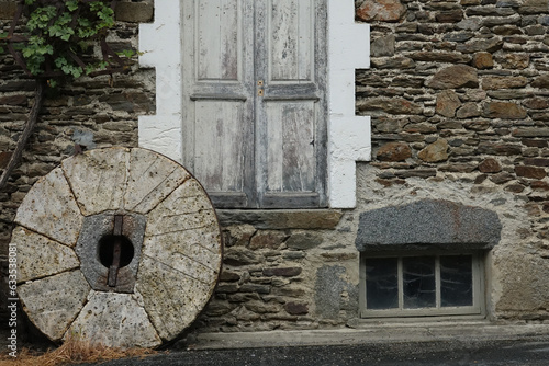 Old stone wheel in front of the wall of an old house made of stones © Sylvain