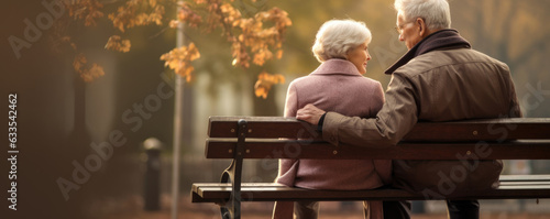 A picture of an elderly couple sitting on a park bench his arm around her shoulder both looking off sadly into the distance.