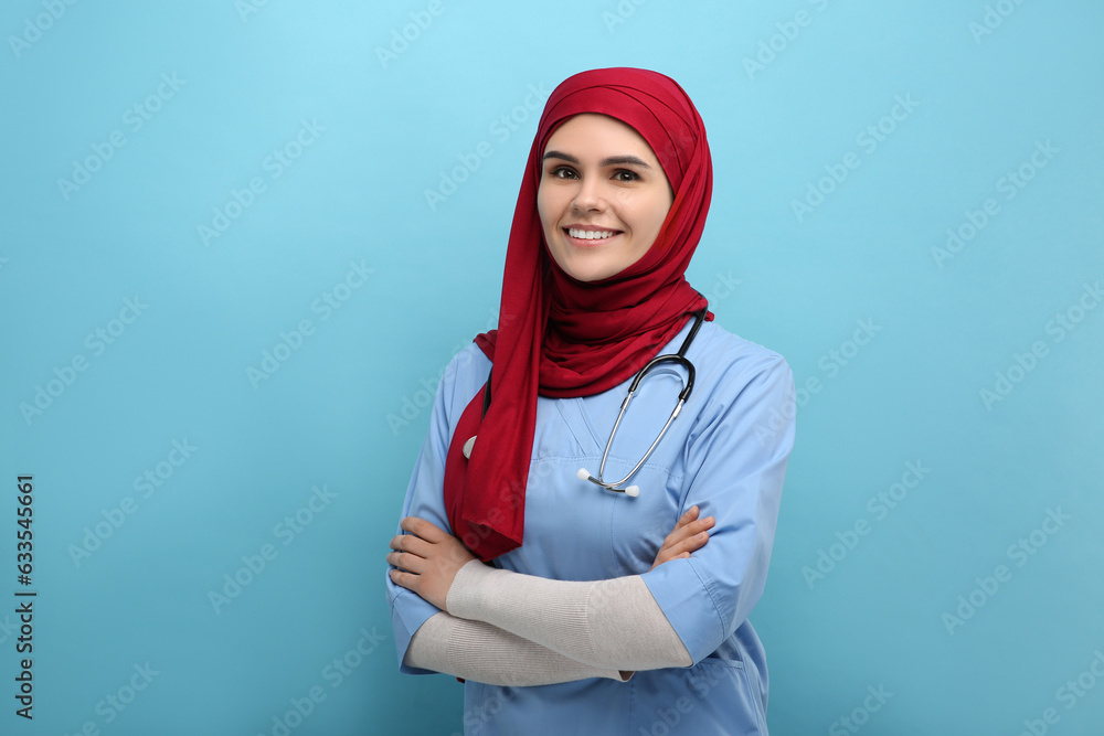 Muslim woman wearing hijab and medical uniform with stethoscope on light blue background Muslim woman wearing hijab and medical uniform with stethoscope on light blue background