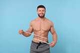 Portrait of happy athletic man measuring waist with tape on light blue background. Weight loss concept