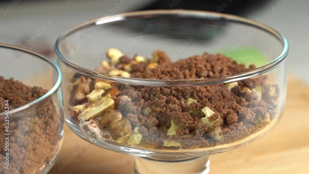 Assembling a puff dessert in a glass bowl with whipping cream cheese and nuts. Cooking at home Assembling a puff dessert in a glass bowl with whipping cream cheese and nuts. Cooking at home