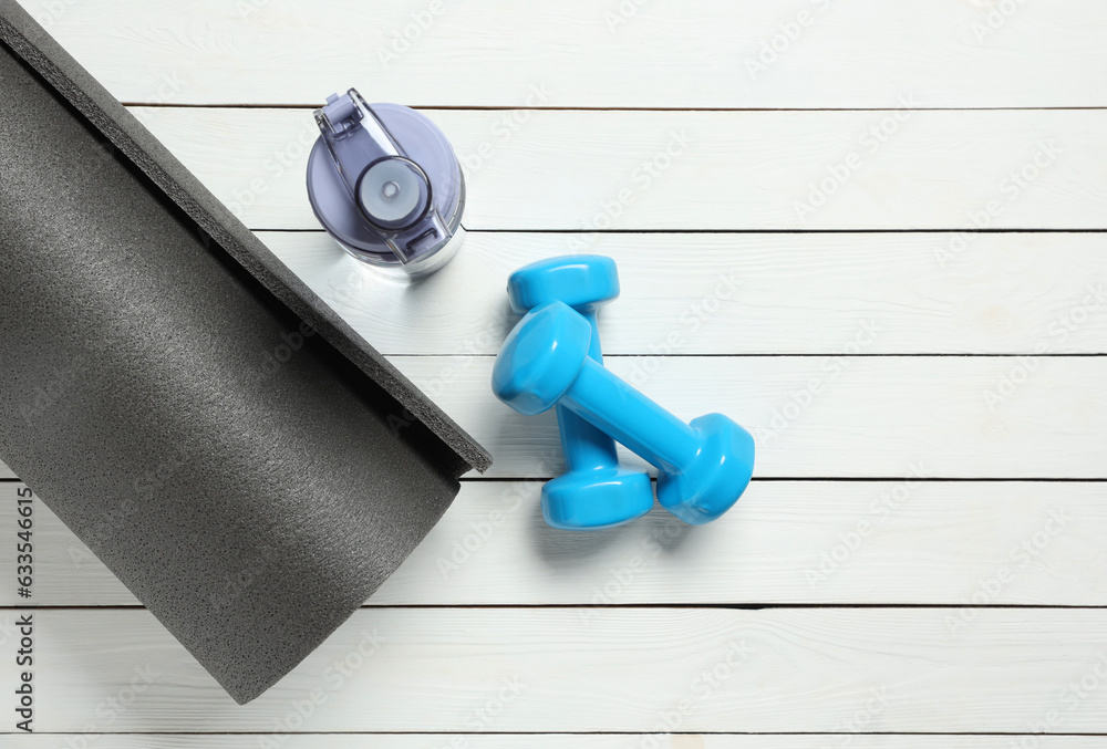 Yoga mat, dumbbells and bottle of water on white wooden floor, flat lay. Space for text Yoga mat, dumbbells and bottle of water on white wooden floor, flat lay. Space for text