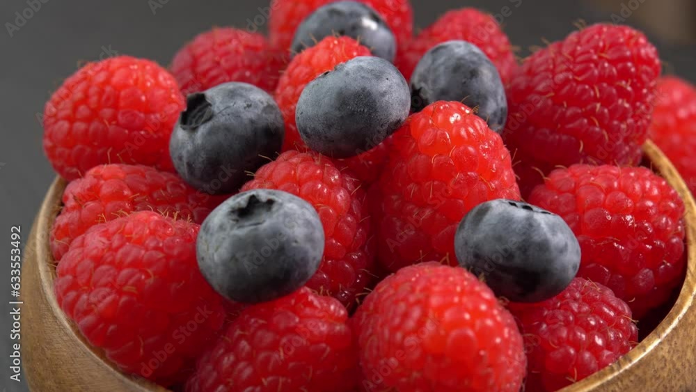 Ripe raspberries and blueberry close up rotate in a wooden bowl. Juicy fresh blueberry and raspberry berry is healthy and contains vitamins and nutrients Ripe raspberries and blueberry close up rotate in a wooden bowl. Juicy fresh blueberry and raspberry berry is healthy and contains vitamins and nutrients