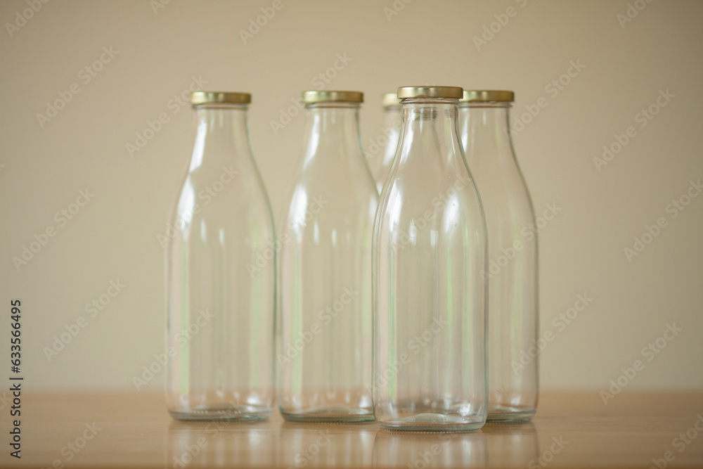 Several empty glass bottles for milk standing on the wooden table over light beige background. Day light. Indoor shot Several empty glass bottles for milk standing on the wooden table over light beige background. Day light. Indoor shot