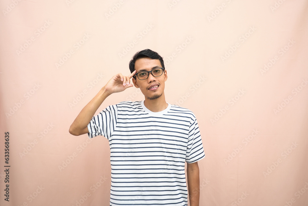 Asian man in glasses wearing casual striped t-shirt, gesturing get ideas, looking for ideas, thinking. Isolated beige background. Asian man in glasses wearing casual striped t-shirt, gesturing get ideas, looking for ideas, thinking. Isolated beige background.