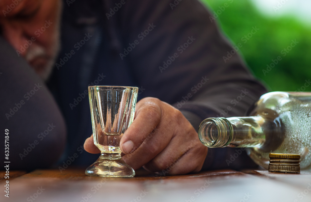 Ein Mann schläft betrunken an einem Tisch. Eine leere Flasche und ein Schnapsglas sind vor ihm. - obrazy, fototapety, plakaty 
