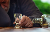 Ein Mann schläft betrunken an einem Tisch. Eine leere Flasche und ein Schnapsglas sind vor ihm.