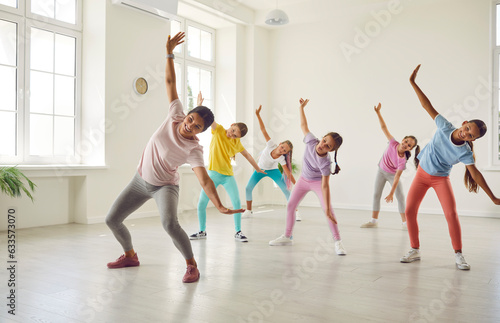Smiling friendly choreographer showing her students girls dance exercises in studio. Happy children training in a group choreography class doing dance workout and learning modern dances.