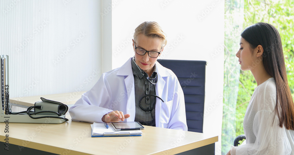 Asian woman patient sitting with doctor about her illness and showing x-ray results with blood pressure and heart rate measurement with stethoscope Asian woman patient sitting with doctor about her illness and showing x-ray results with blood pressure and heart rate measurement with stethoscope