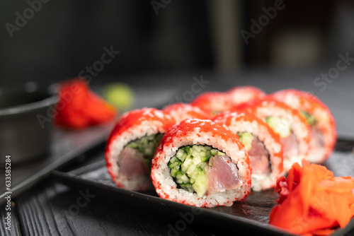 Delicious sushi roll california with tuna cucumber cheese and masago caviar on top on a stone plate on black background.